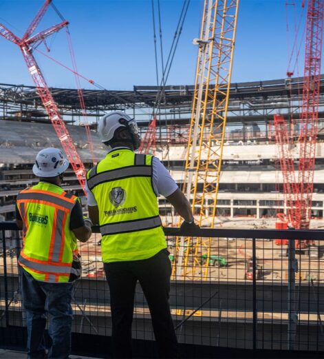 Construction workers in safety vests and helmets overlooking a stadium build site